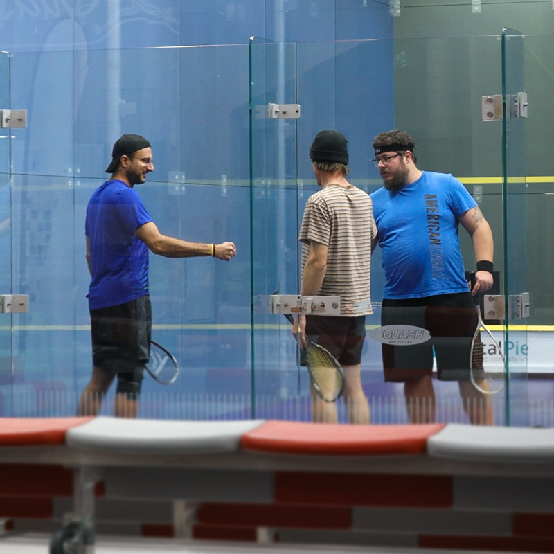 3 males fist-bumping during a squash game