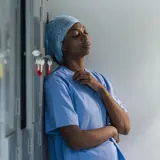 a surgical staff leaning against a wall feeling tired